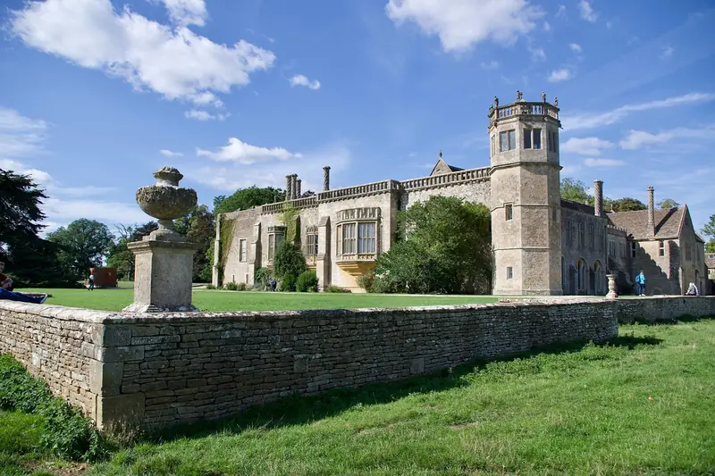 Lacock Abbey's stone frontage and octagonal tower behind a low wall and lawn