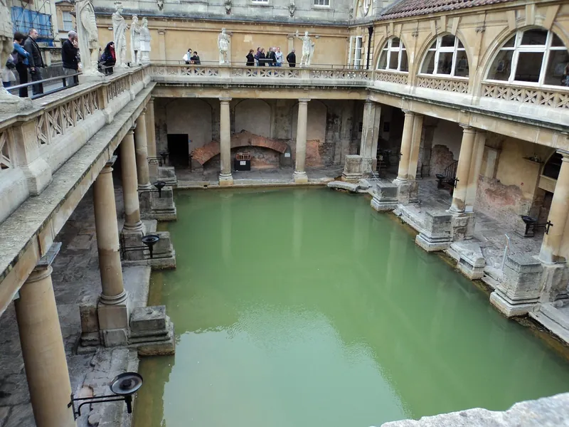 The green water of the Great Bath at the Roman Baths, ringed by stone columns and a terrace of statues