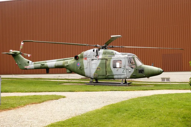 A camouflaged Westland Lynx helicopter displayed on the grass outside an aviation museum