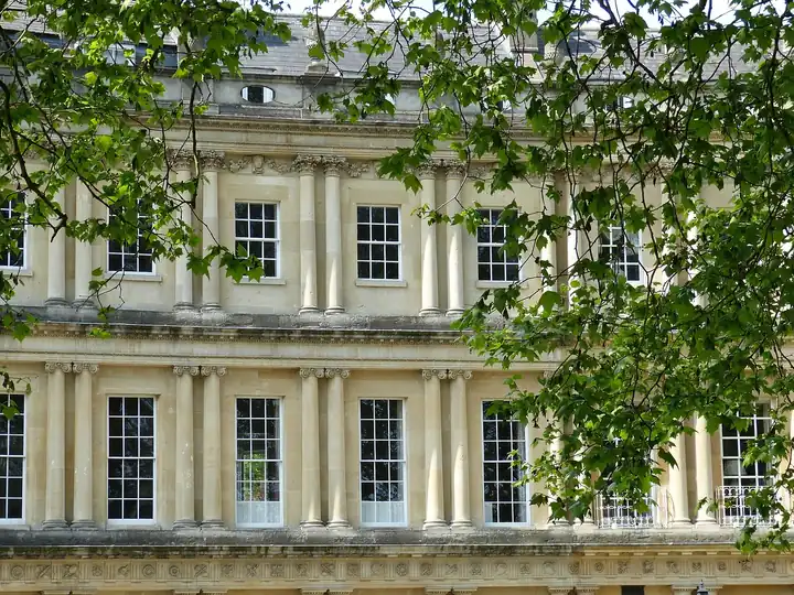Pale stone Georgian facade with columns, a deep cornice and a parapet with slate roof just visible behind