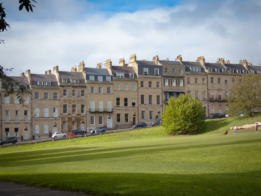 Long Georgian stone terrace with parapets and rows of chimney stacks above a sloping green