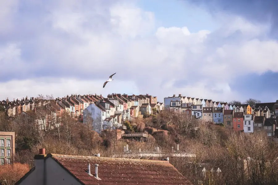 Brightly painted terraced houses stepping up a steep wooded hillside under a cloudy sky