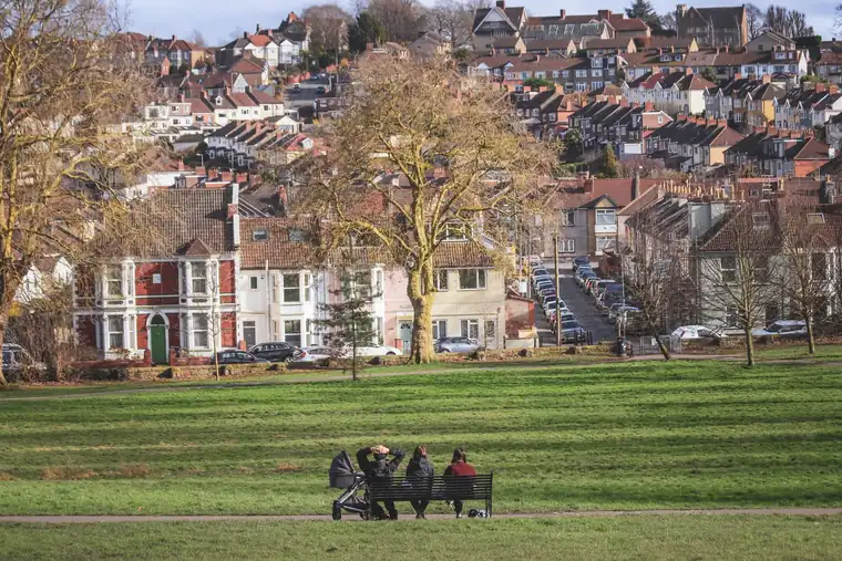 Victorian houses with front gables and bay windows on a hillside above a park with bare trees